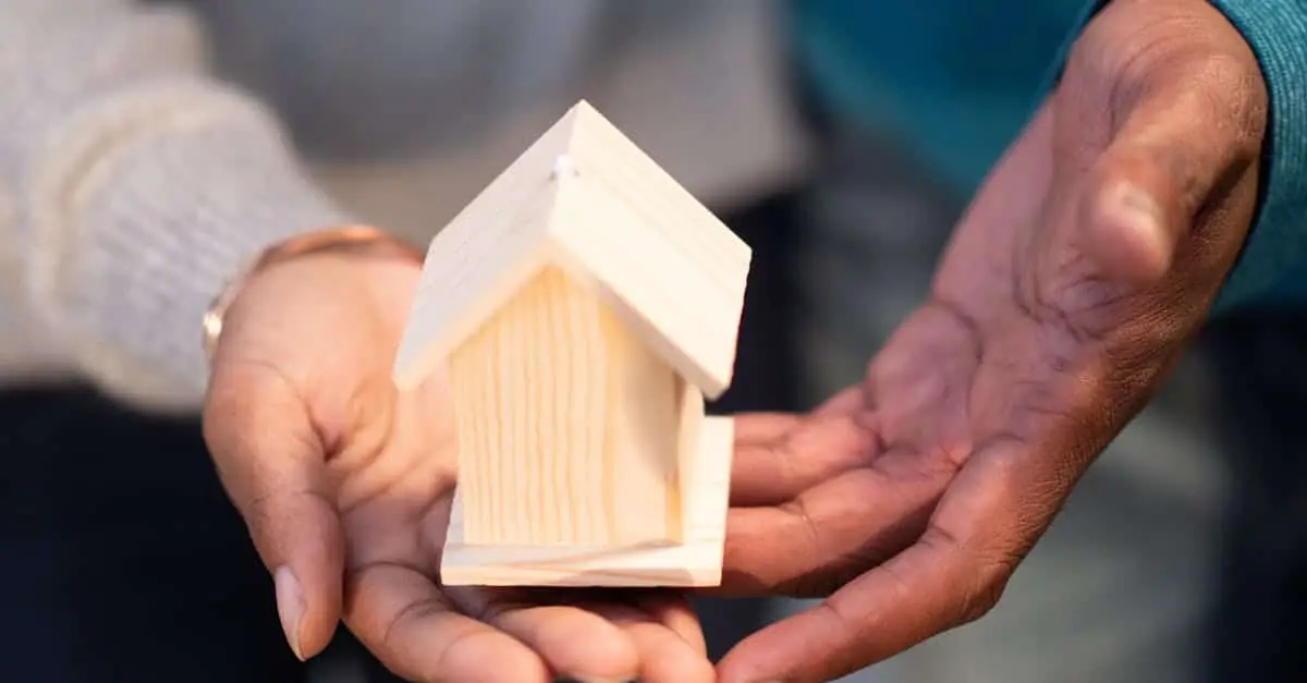 Hands holding a small wooden house model, symbolizing new home ownership and real estate transactions.